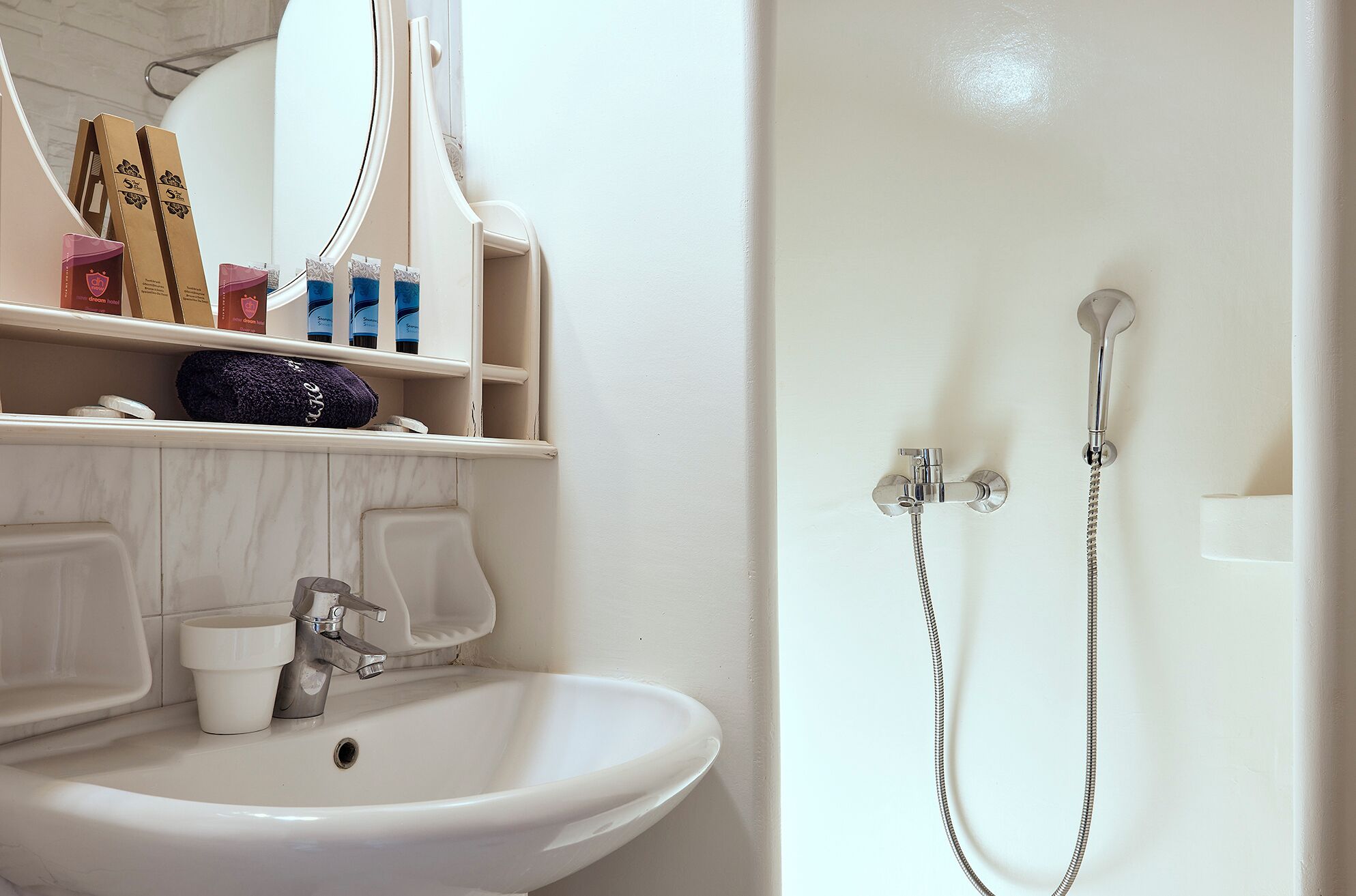 A bathroom with a white sink, mirror, and shower. There are toiletries on the shelf.