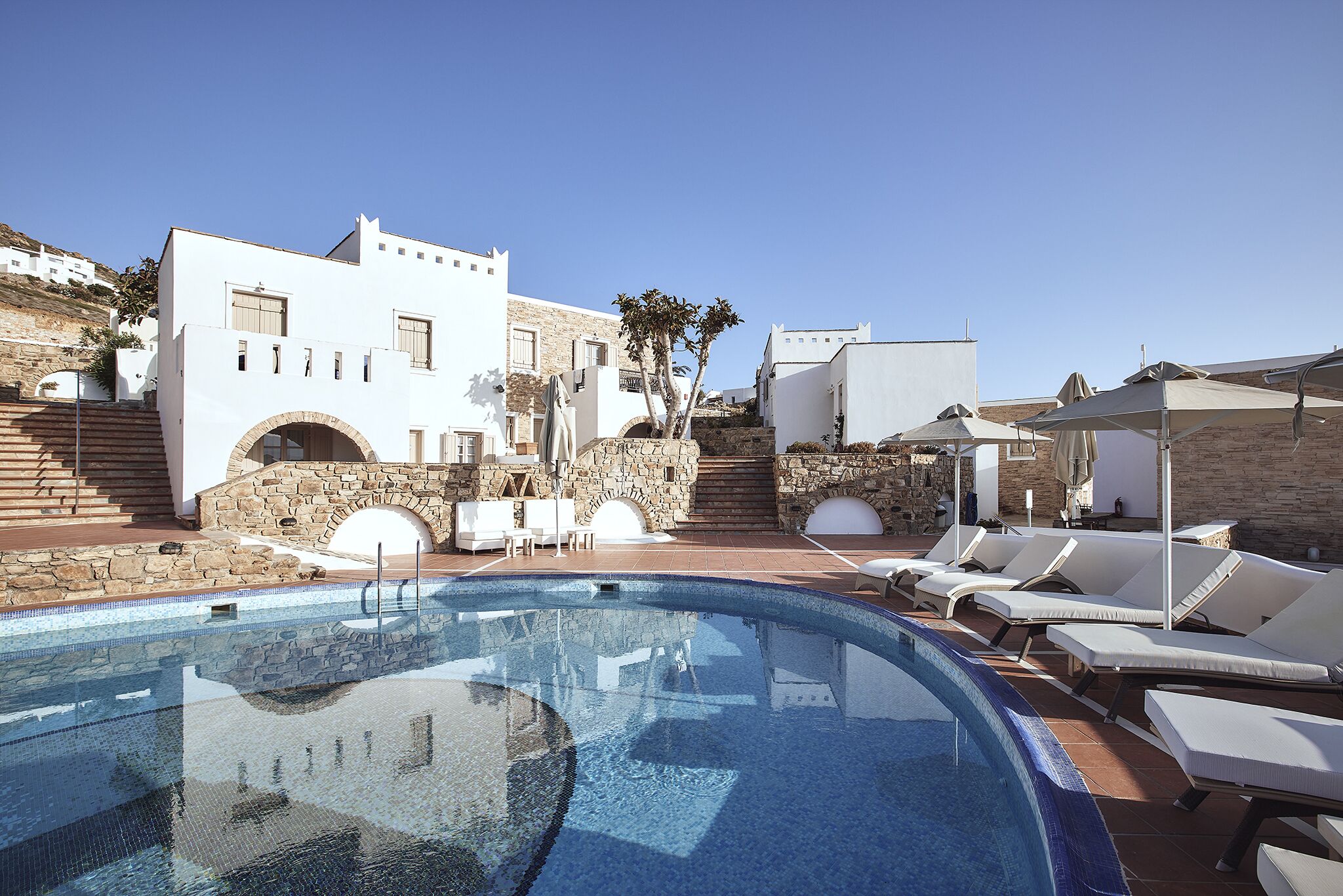 A pool area with lounge chairs and a stone staircase leading to a building.