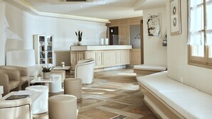 A modern living room with a sofa, ottomans, a coffee table, and a bookshelf. - Naxos Magic Village Hotel (Naxos)