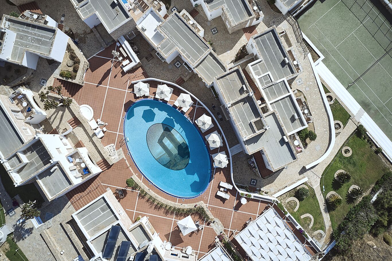 Vue aérienne d’un hôtel doté d’une piscine centrale, de nombreux balcons et d’un court de tennis.