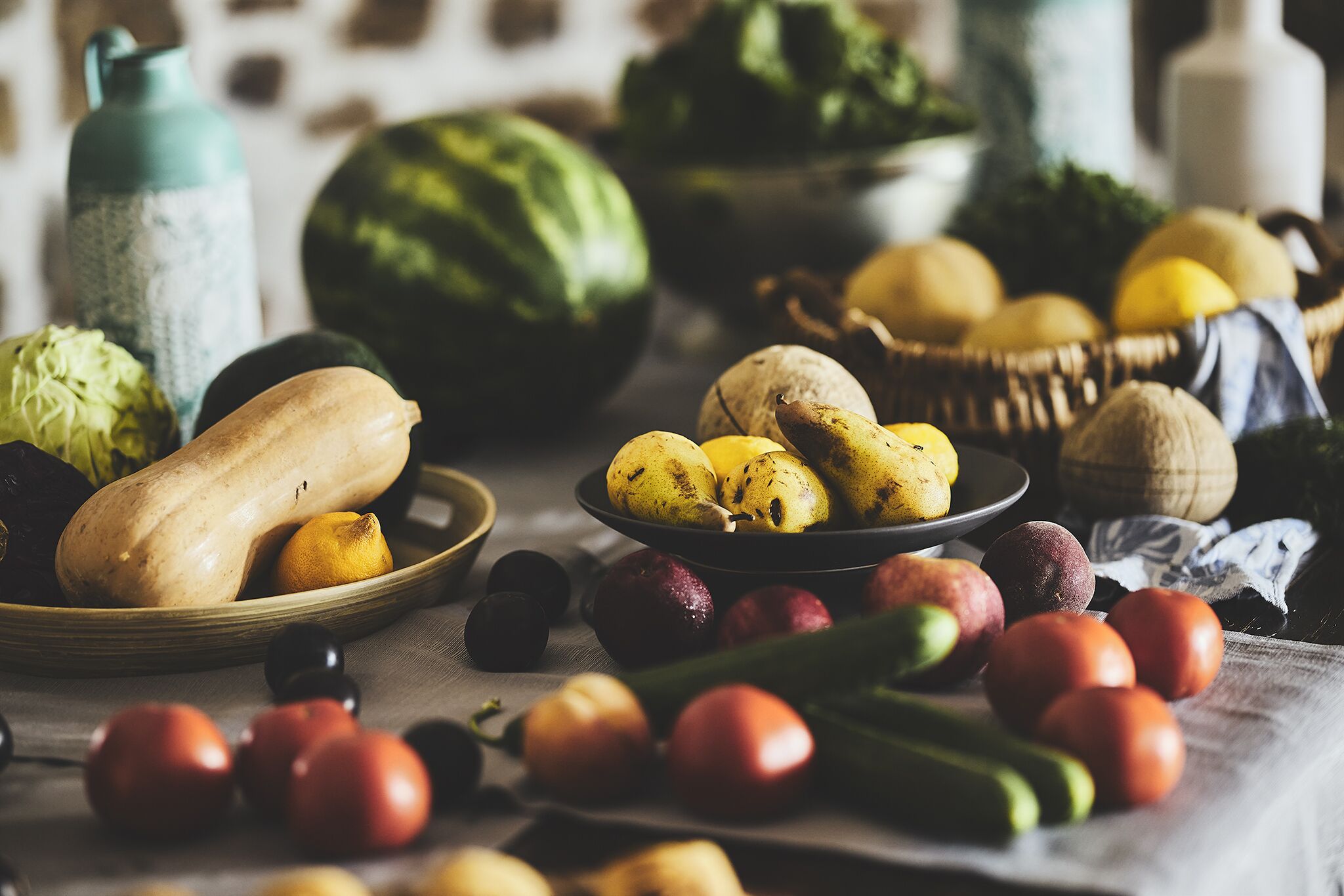 Una variedad de frutas y verduras sobre una mesa, incluyendo manzanas, tomates y una sandía.