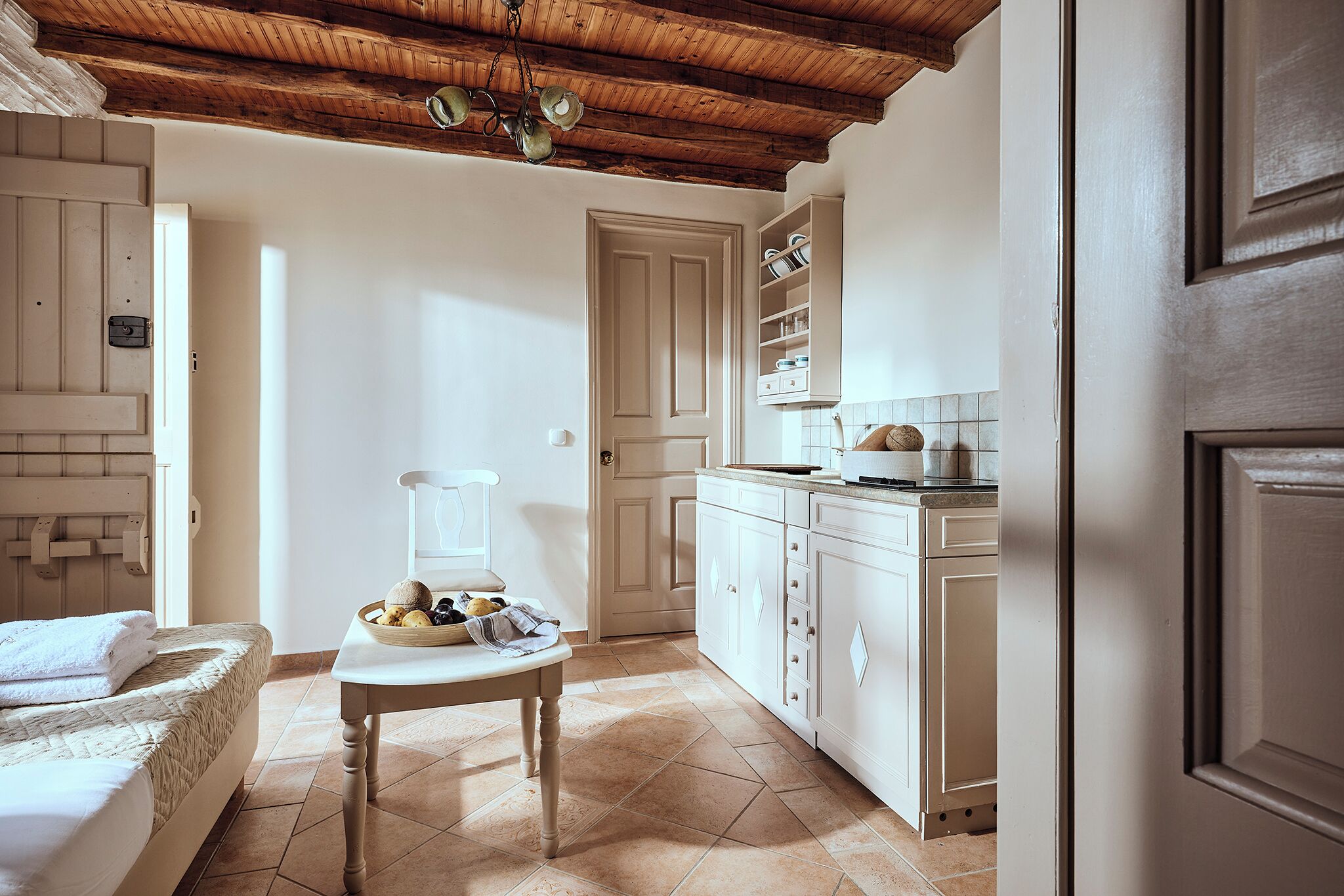 A compact kitchen with white cabinets, a wooden ceiling, and a tiled floor.
