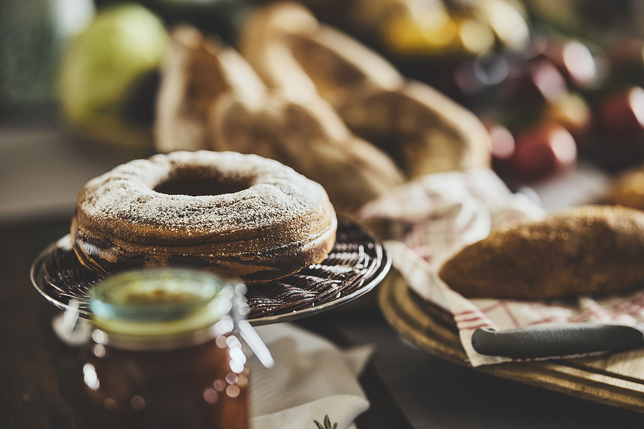A close-up of a cake on a plate, with a knife and a jar of jam nearby.