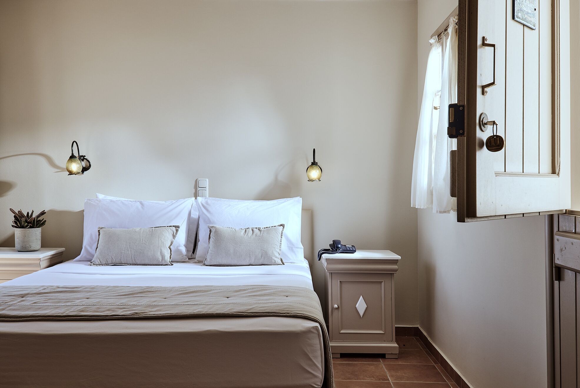 A bedroom with a bed, bedside tables, a nightstand, a lamp, a potted plant, and a wardrobe.