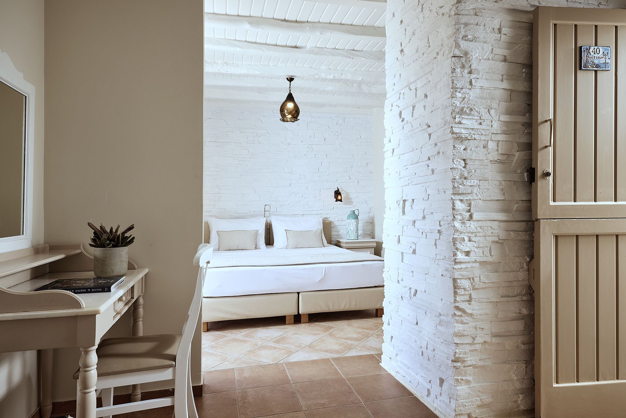A bedroom with a bed, bedside table, lamp, and a white brick wall.