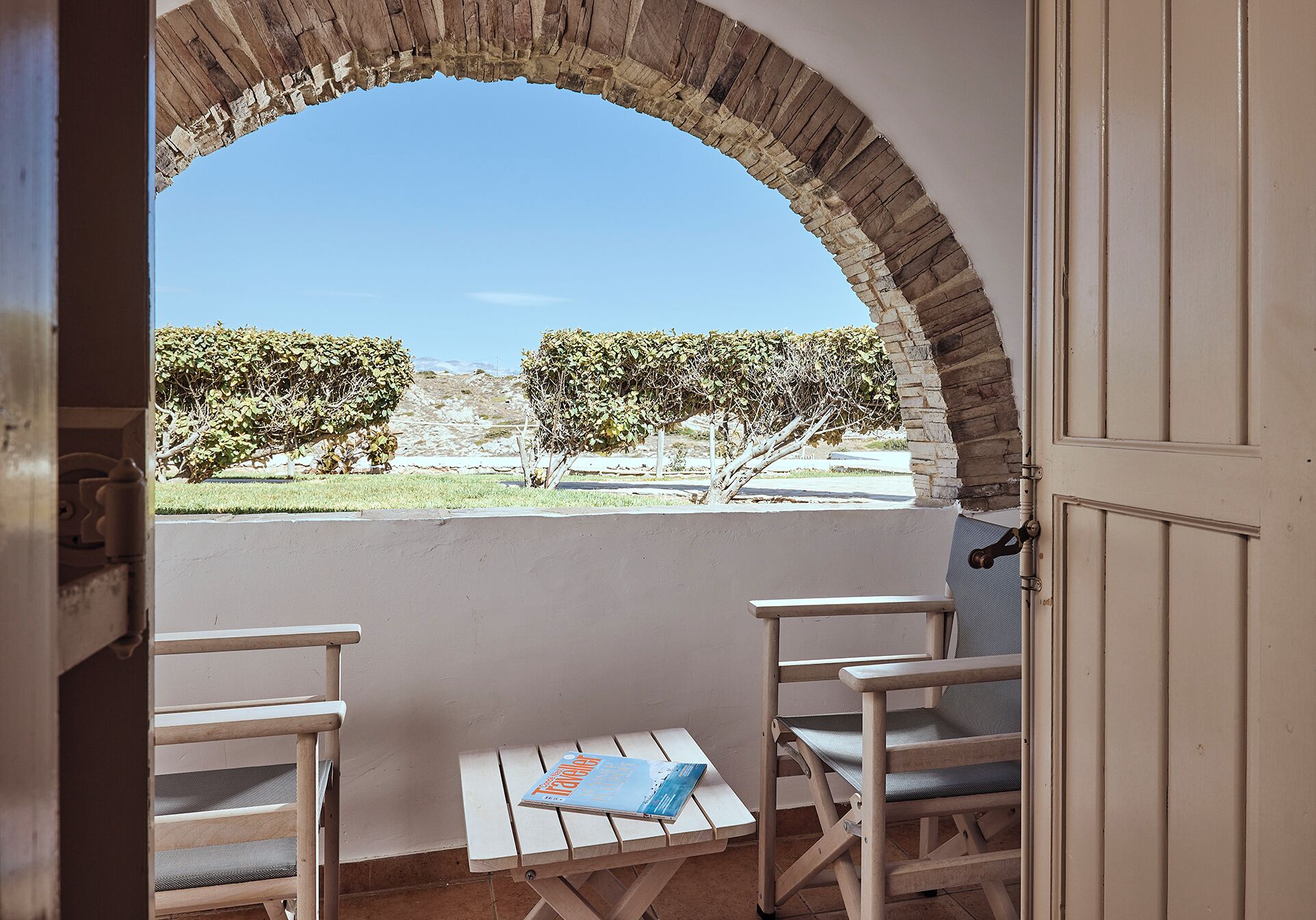 Un espacio al aire libre con zona de estar y vistas a través de un arco, que incluye una mesa pequeña y dos sillas.