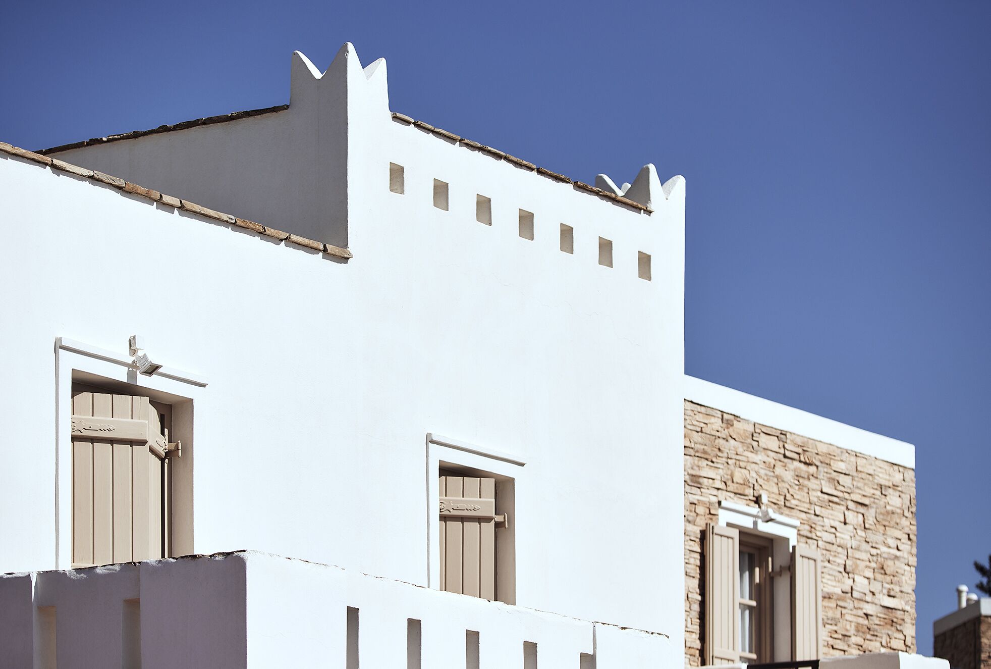 A building with a white facade, a stone wall section, and a flat roof.