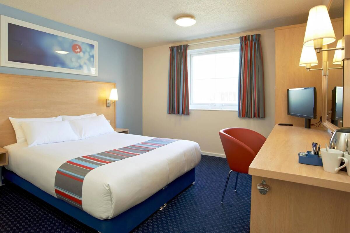 A hotel room with a bed, a desk, a chair, a television, and a window with curtains.
