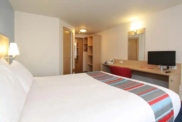 A hotel room with a bed, a desk with a computer, a mirror, and a door leading to a bathroom.