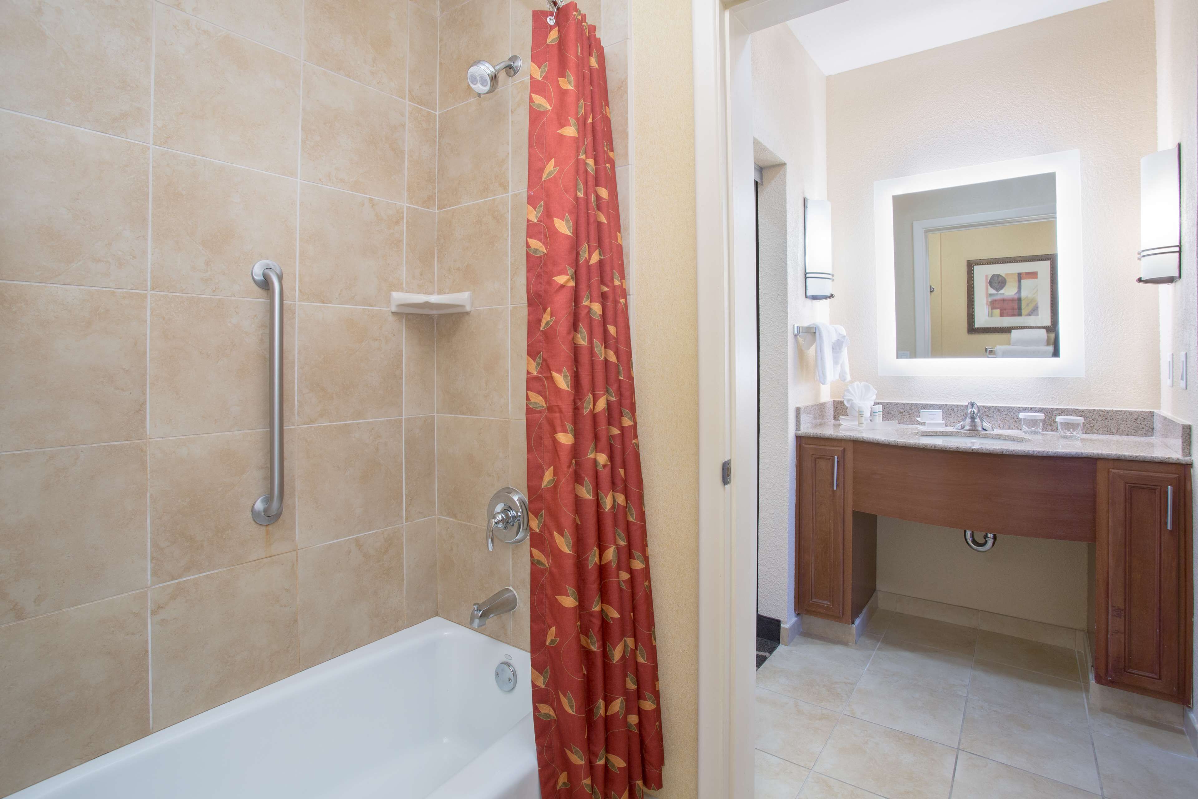 Une salle de bain comprenant une baignoire, une douche avec une barre d’appui, un meuble-lavabo avec un miroir et des toilettes.