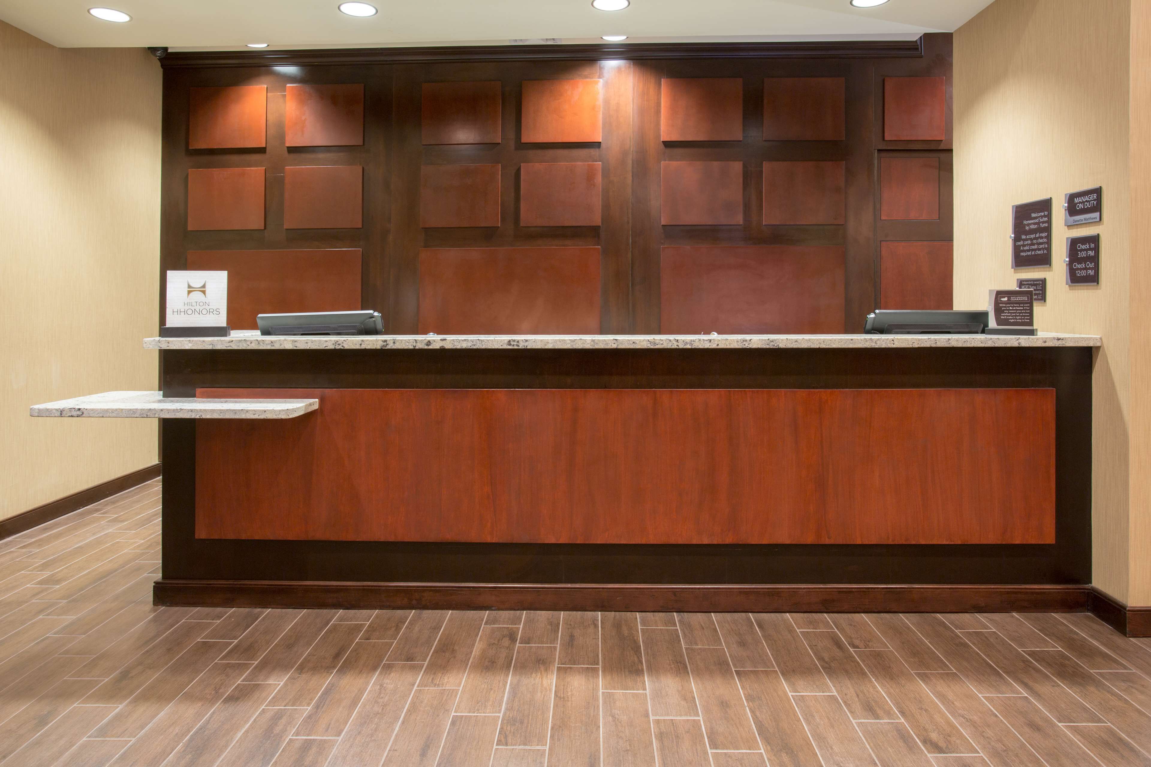 A hotel reception desk with a wooden panel design, a sign indicating the hotel name, and a check-in counter.