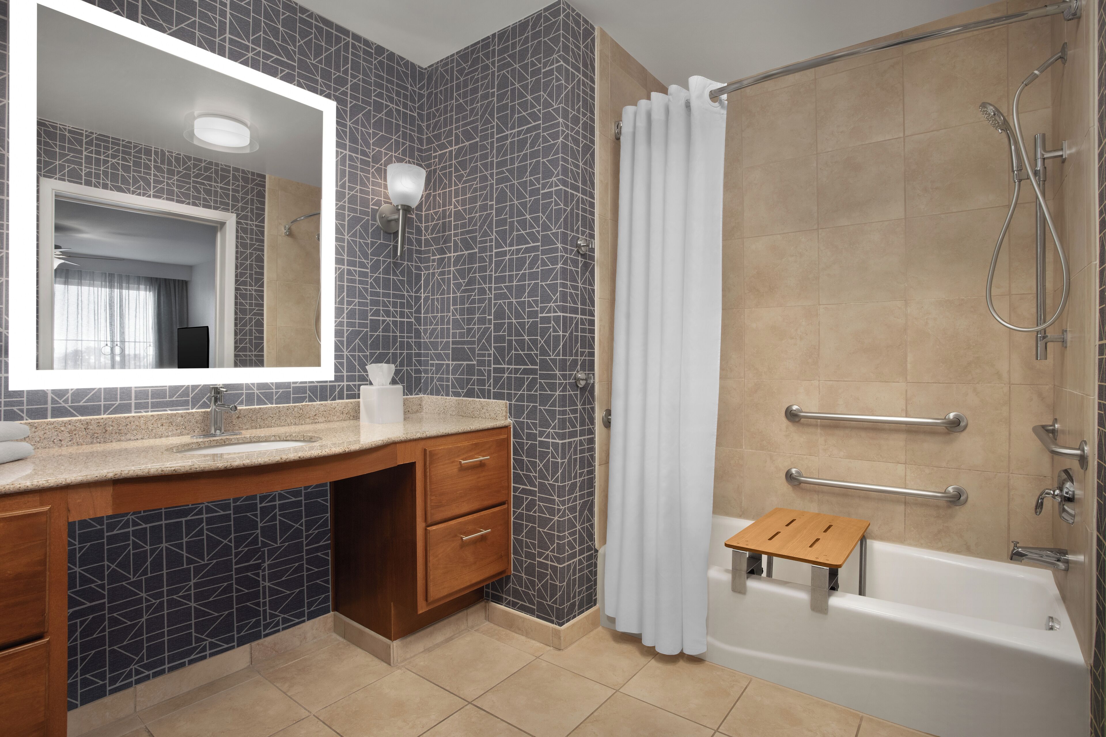 A modern bathroom with a large mirror, a sink, a shower, and a small wooden stool.