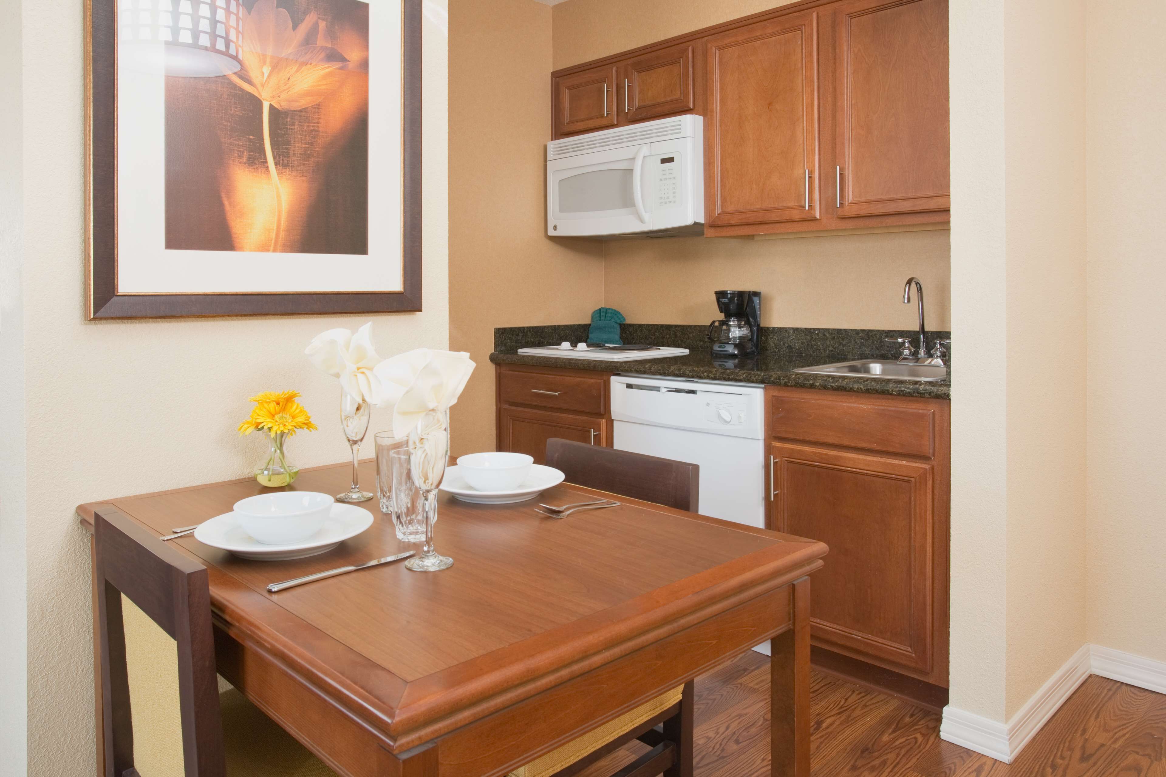 A dining area with a wooden table set for two, a microwave above the counter, and a sink.