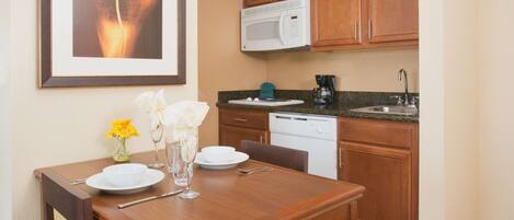 A dining area with a wooden table set for two, a microwave above the counter, and a sink.
