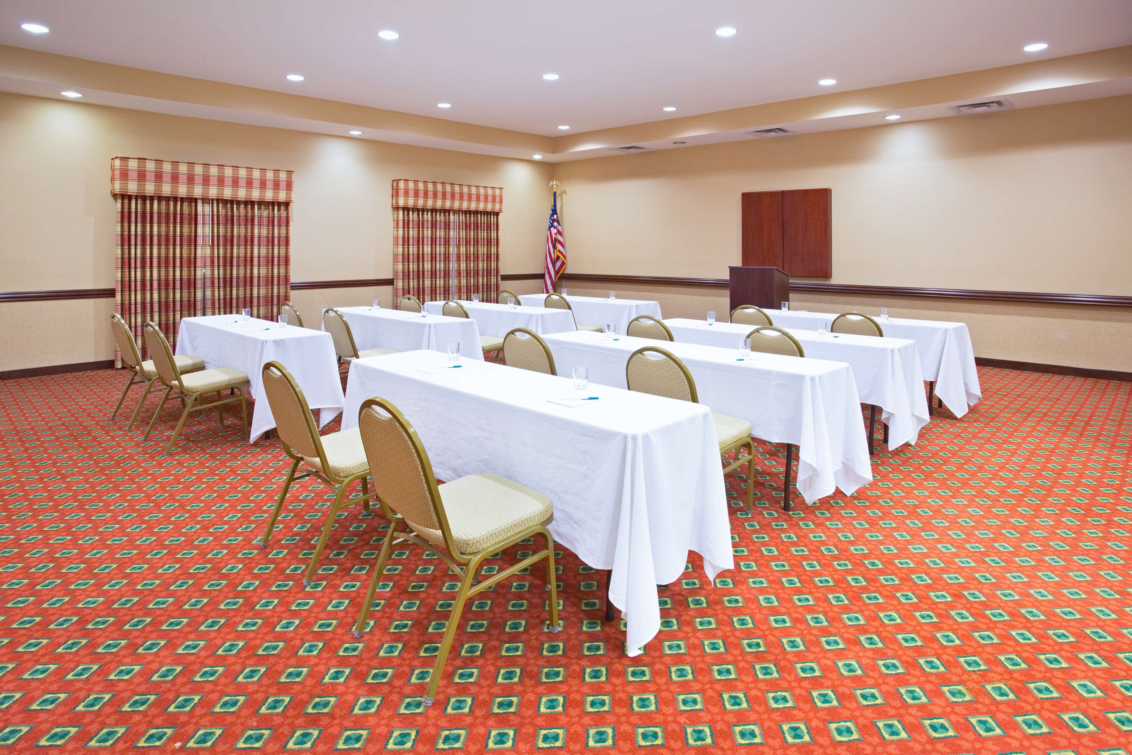 Ein Konferenzraum mit mehreren Tischen, Stühlen, einer amerikanischen Flagge und einem gemusterten Teppich.