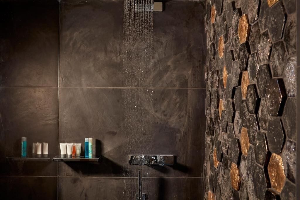 A shower with a stone wall and a shelf with toiletries.