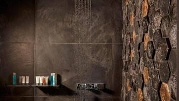 A shower with a stone wall and a shelf with toiletries.