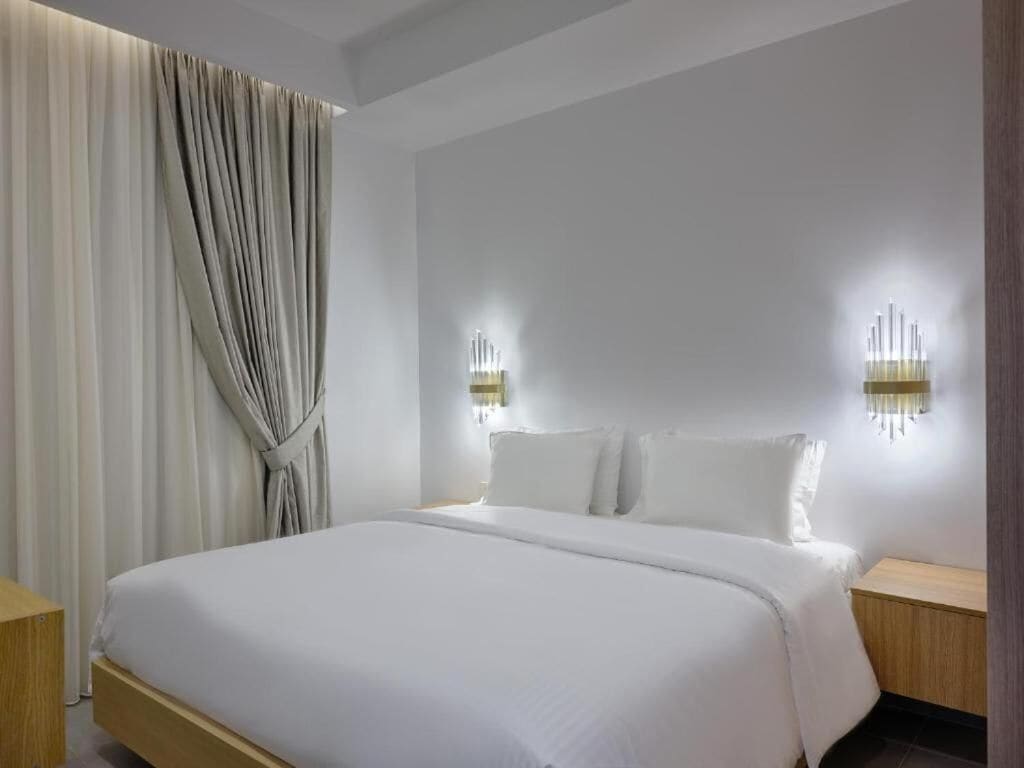 A hotel room with a large bed, two bedside tables, and a wall-mounted light fixture.