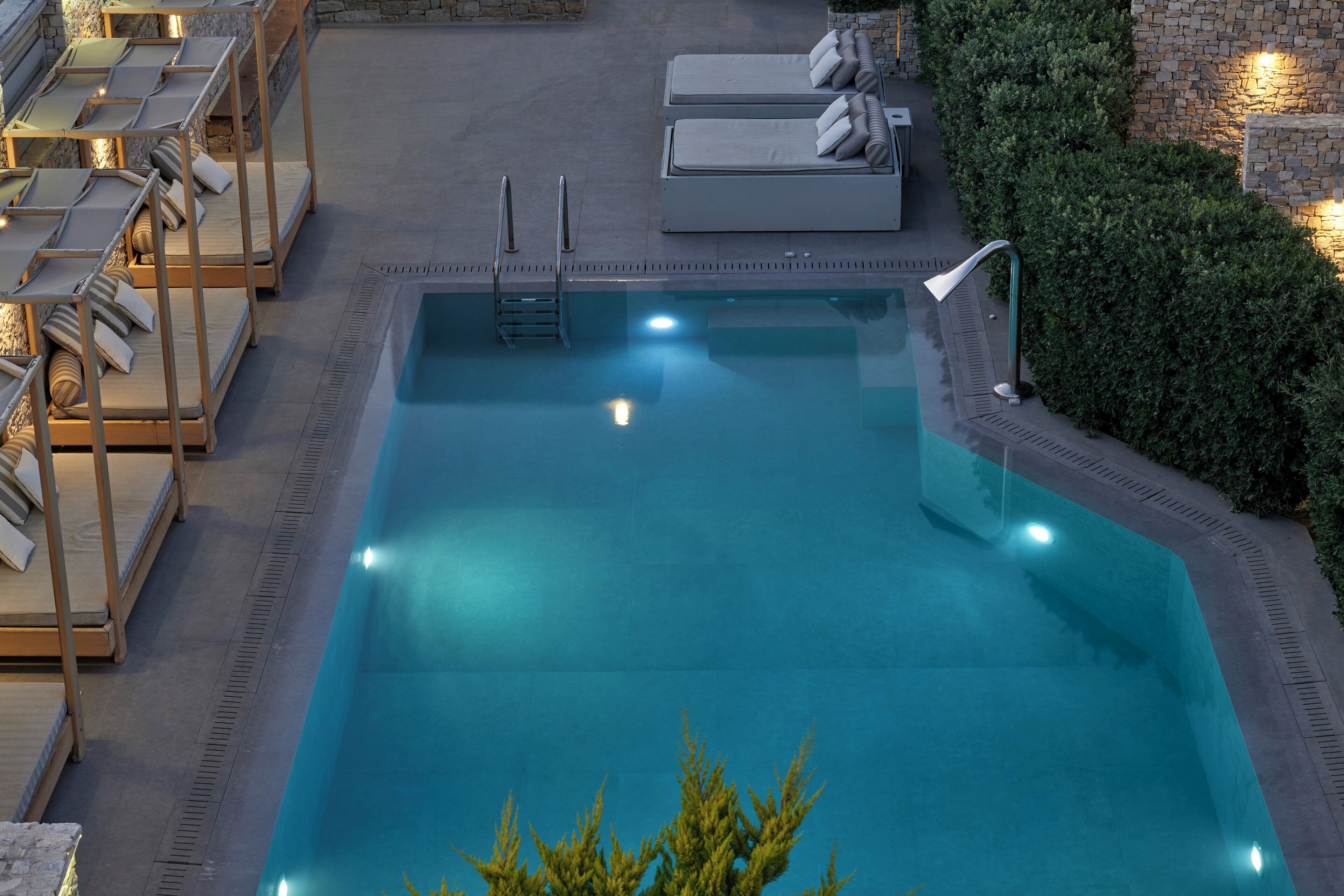Une piscine rectangulaire, dotée d’un escalier et de marches, entourée de chaises longues et d’un mur en pierre.