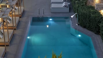 Une piscine rectangulaire, dotée d’un escalier et de marches, entourée de chaises longues et d’un mur en pierre.