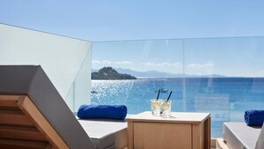 Un balcón con vistas despejadas al mar, una silla de madera, una mesita con bebidas y una toalla azul.