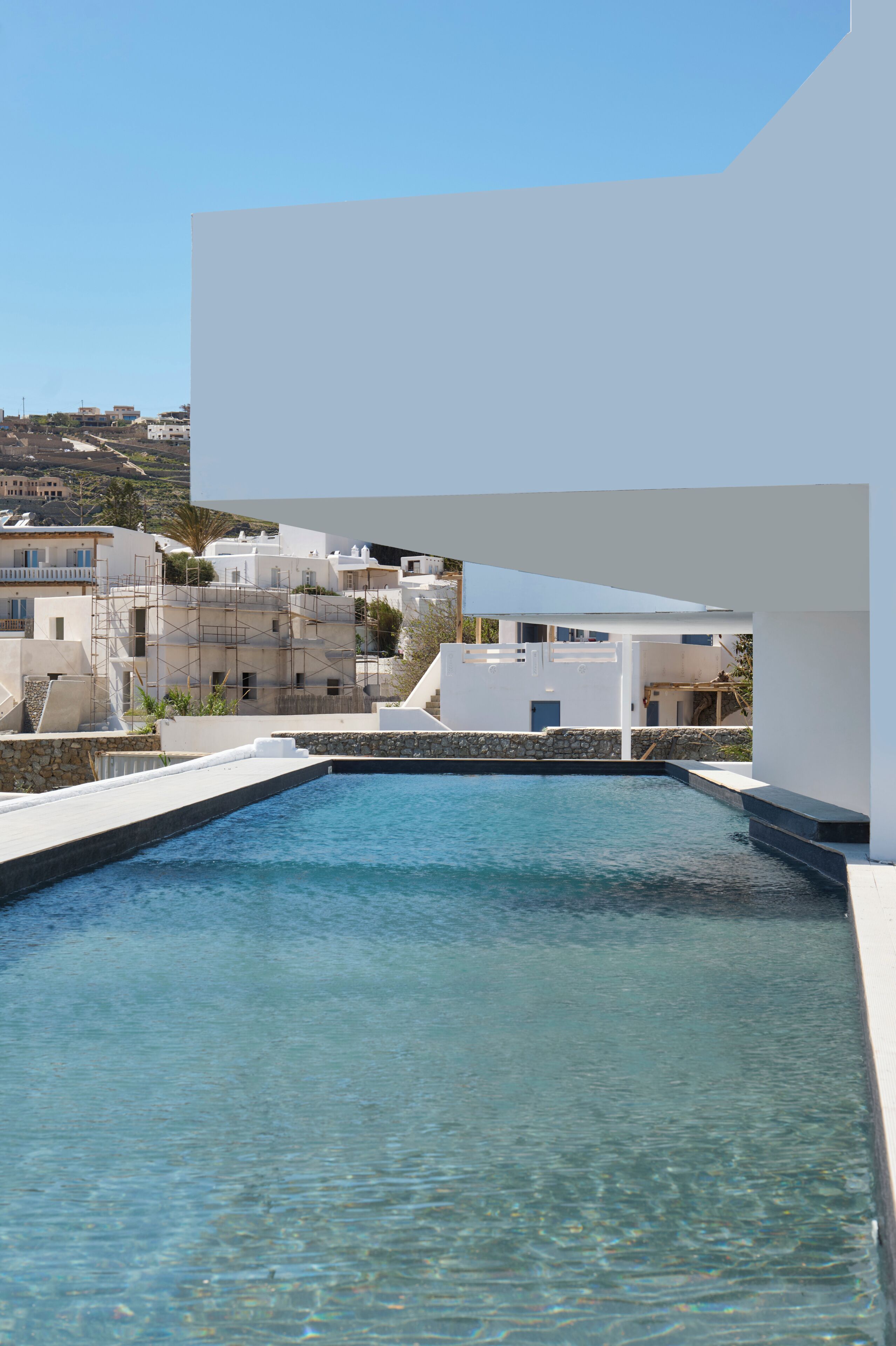 A pool with clear water, surrounded by white buildings and a stone wall.