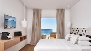 Un hotel moderno con una cama grande, una mesita de noche de madera con una cafetera, vistas al mar y una silla de playa fuera de la ventana.