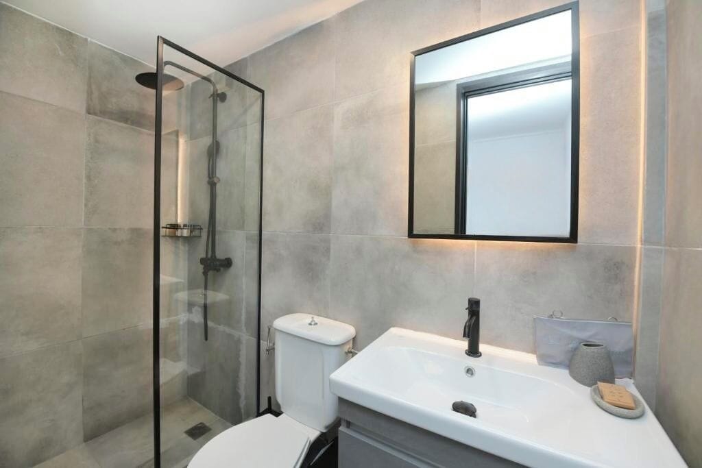 Ein modernes Badezimmer mit einer begehbaren Glasdusche, einem weißen Waschbecken und einem Spiegel darüber.