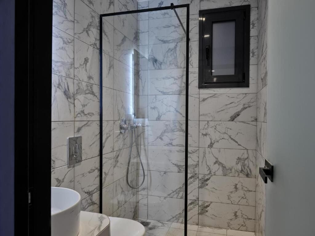 Une salle de bain avec une douche à parois de verre, un lavabo blanc et des murs à motifs de marbre.