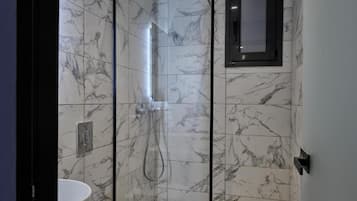 Une salle de bain avec une douche à parois de verre, un lavabo blanc et des murs à motifs de marbre.