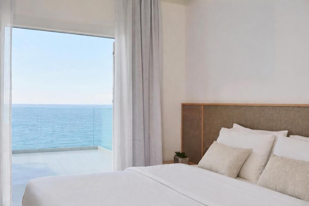 A hotel room with a large bed, a view of the sea, and a balcony.