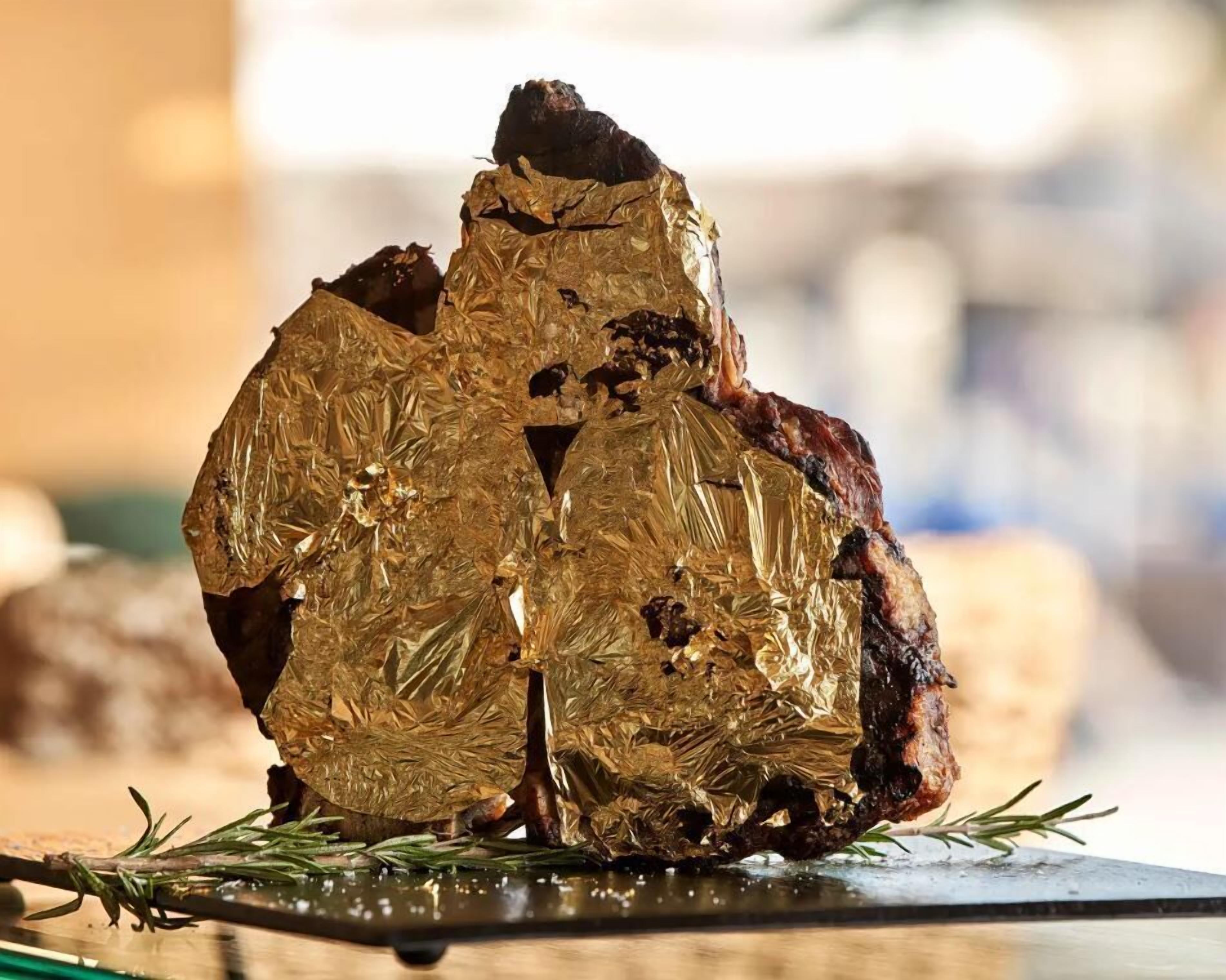 A roasted meat with foil wrapping, placed on a wooden board with rosemary sprigs.