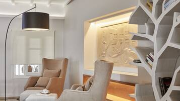 A modern living room with two beige armchairs, a floor lamp, and a unique wooden bookshelf.
