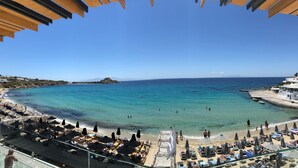 Una playa con tumbonas y sombrillas, mar azul cristalino y un litoral rocoso.