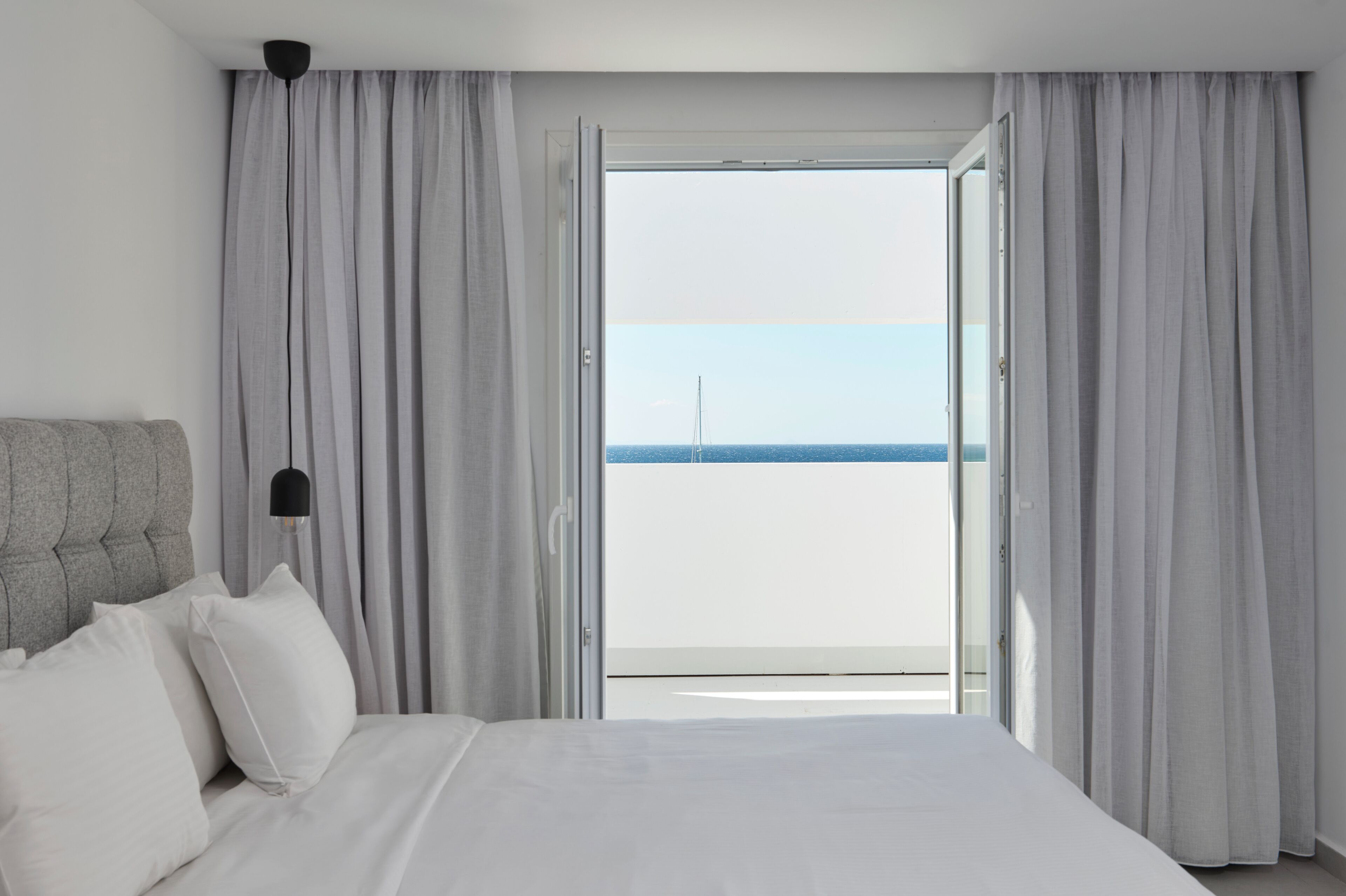 Una habitación de hotel con cama, cortinas y vista al mar.