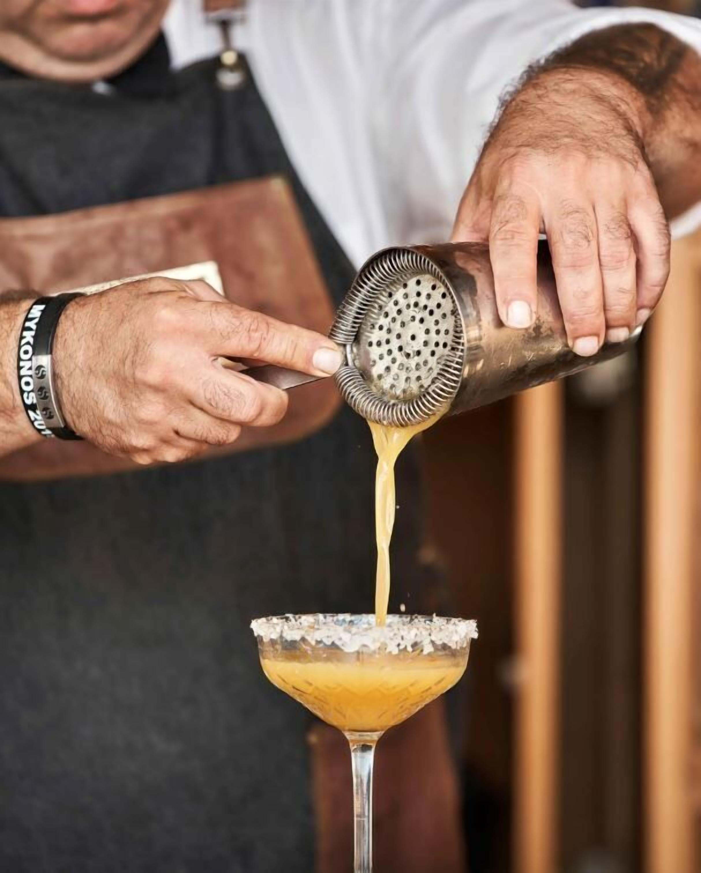 Une personne verse un liquide doré dans un verre dont le bord est saupoudré de sel, ce qui laisse supposer qu’il s’agit d’un cocktail.
