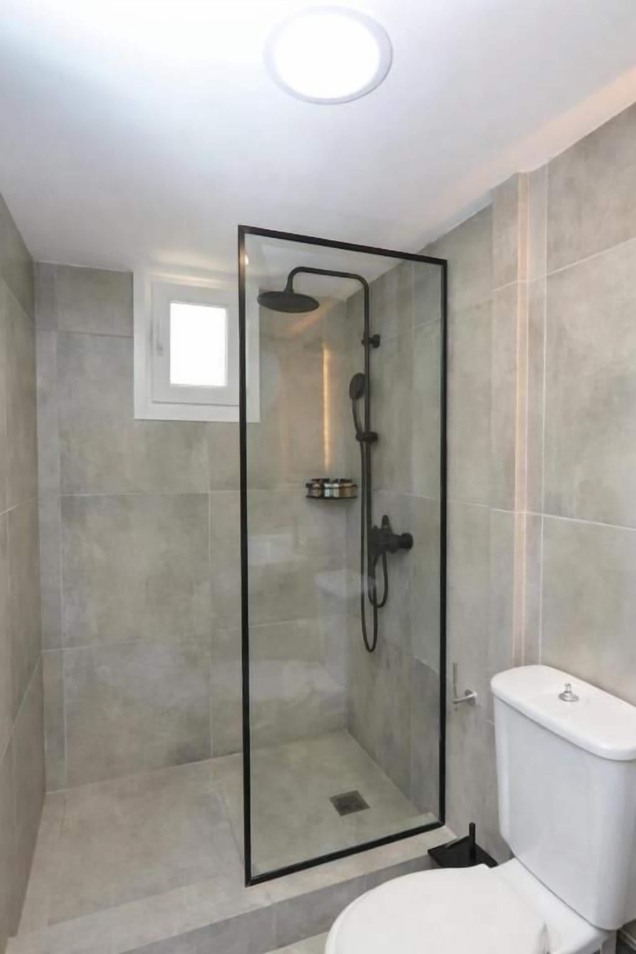A modern bathroom with a glass-enclosed shower, a toilet, and a small window.