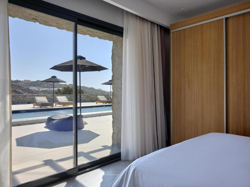 A hotel room with a large sliding glass door leading to a pool area with lounge chairs and umbrellas.