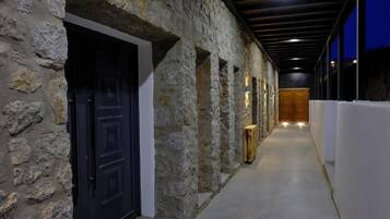 A corridor with stone walls, wooden doors, and a wooden panel wall at the end.