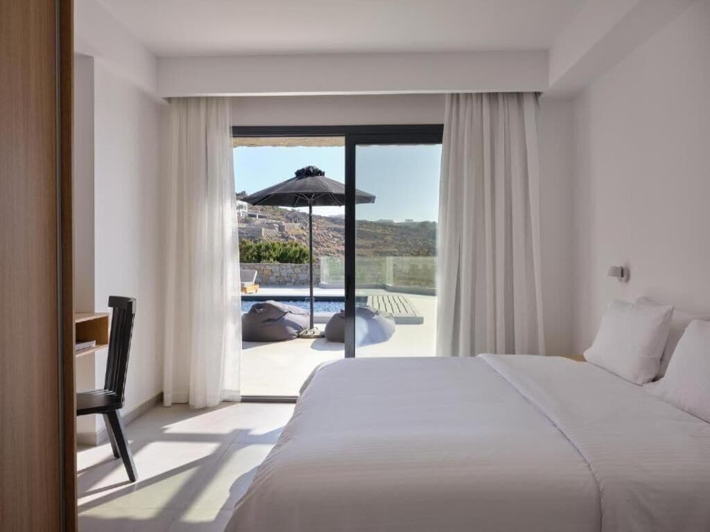 A hotel room with a large bed, a view of a pool and outdoor area, and a sliding glass door.