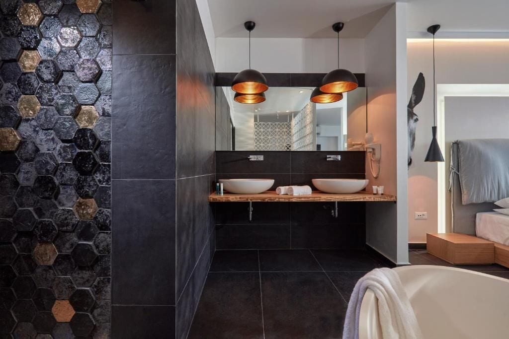 A modern bathroom with a hexagonal tile wall, a wooden vanity with two sinks, and pendant lighting.
