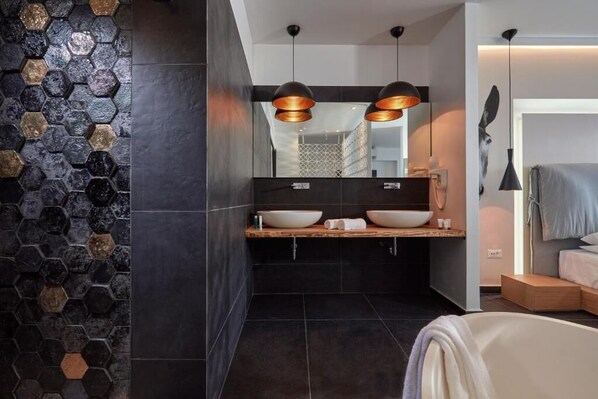 A modern bathroom with a hexagonal tile wall, a wooden vanity with two sinks, and pendant lighting.