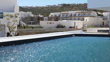 A coastal hotel with white buildings, a swimming pool, and a view of the hillside.