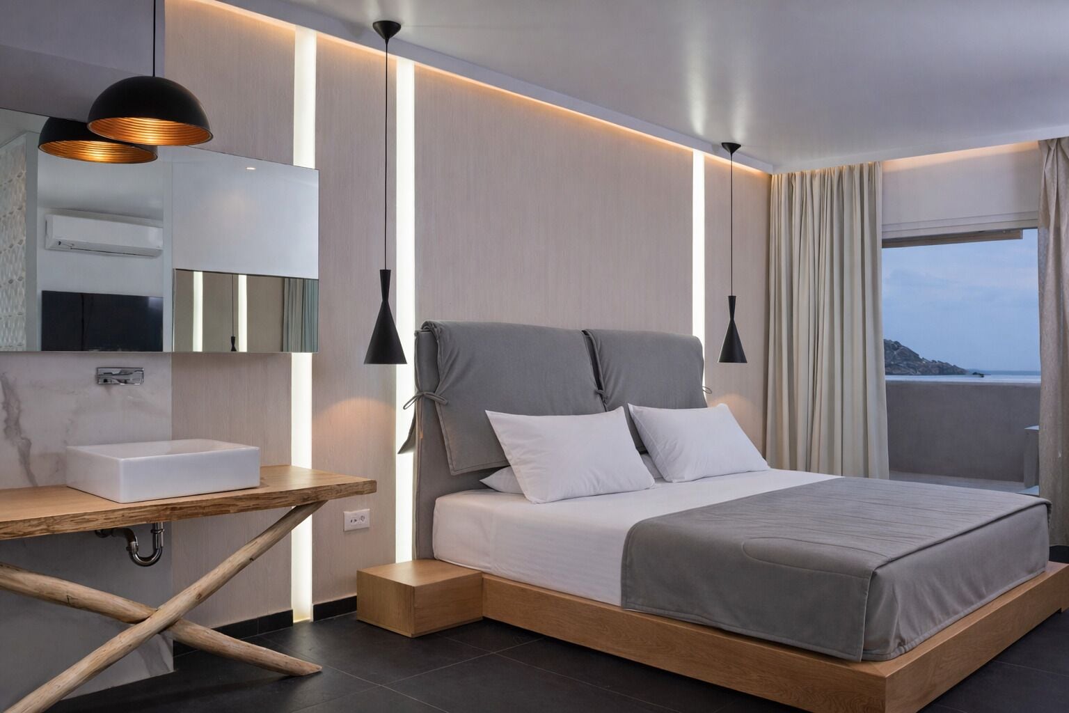 Une chambre d’hôtel moderne, équipée d’un lit, d’une table de chevet et offrant une vue sur la mer.