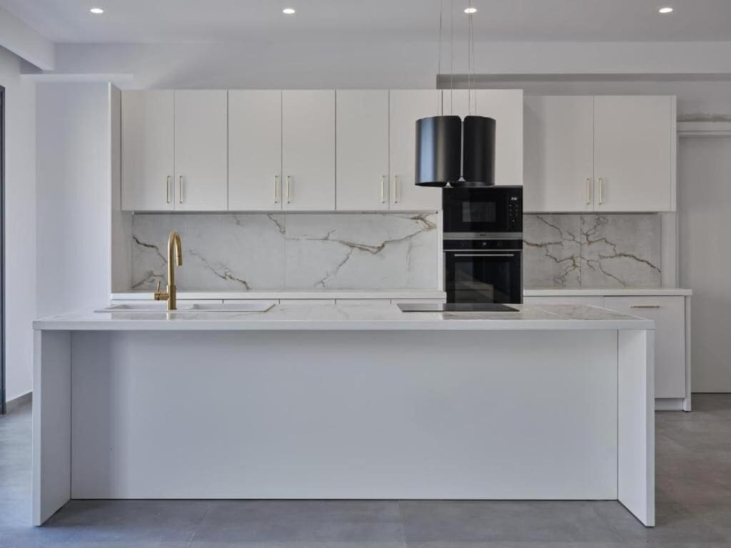 A modern kitchen with white cabinets, a marble backsplash, and a central island with a black coffee machine.