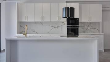 A modern kitchen with white cabinets, a marble backsplash, and a central island with a black coffee machine.