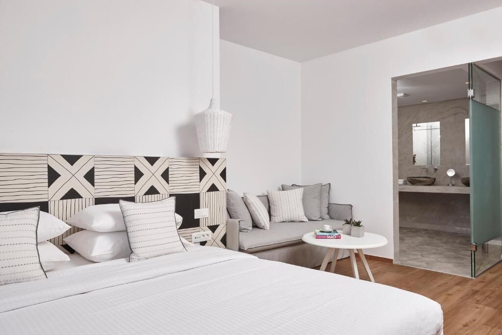 Une chambre moderne comprenant un lit, un canapé, une petite table ronde et une porte en verre donnant sur une salle de bain.