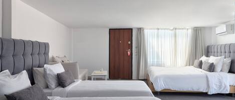 A hotel room with two beds, a small table, a nightstand, a wooden door, and a window with curtains.