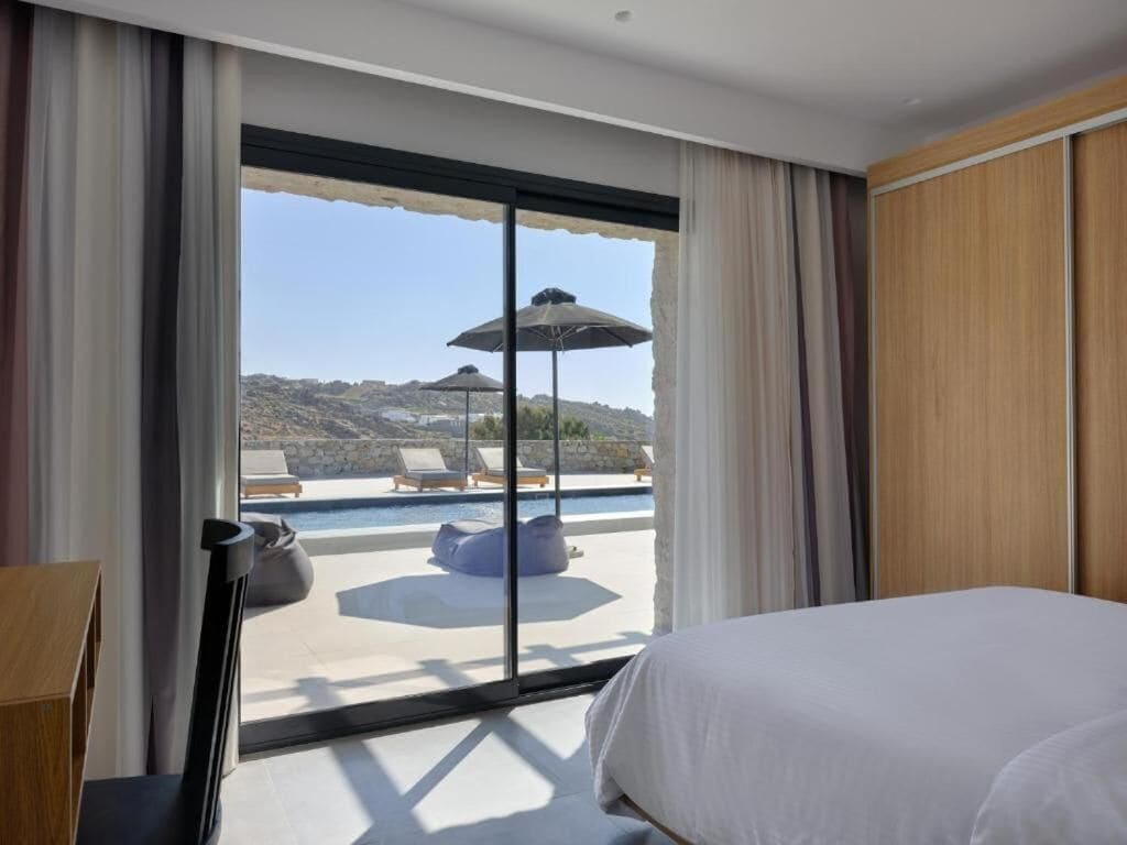 A hotel room with a large bed, a view of a pool and outdoor seating, and a sliding glass door.