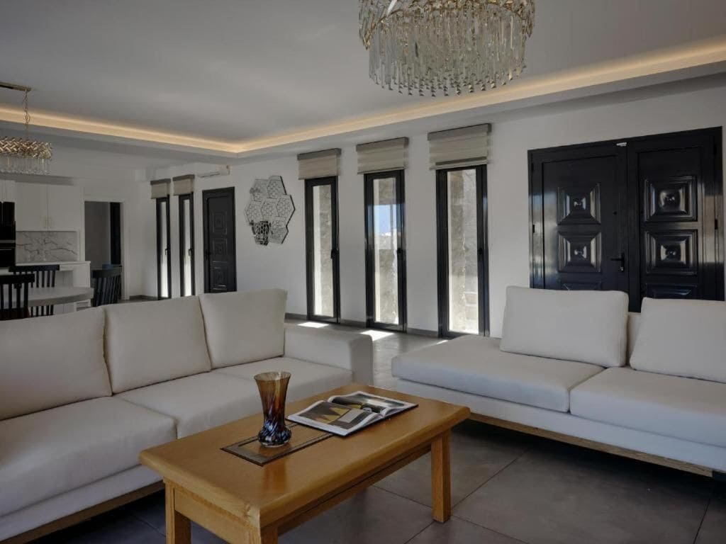 Un salon moderne avec un canapé blanc, une table basse en bois et un lustre.